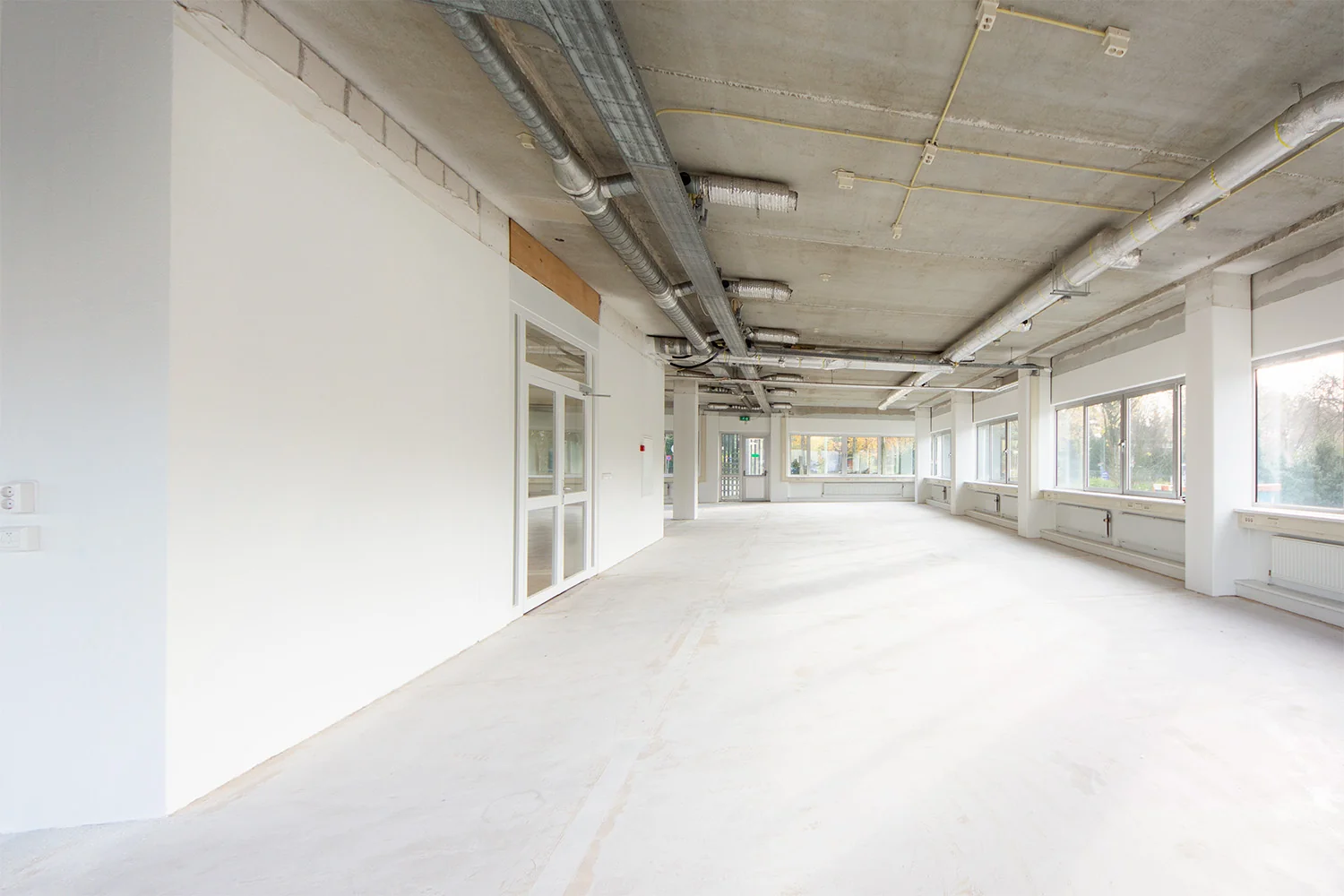 Lichte, lege kantoorruimte aan de Huis-ter-Heideweg met betonnen plafond en grote ramen.